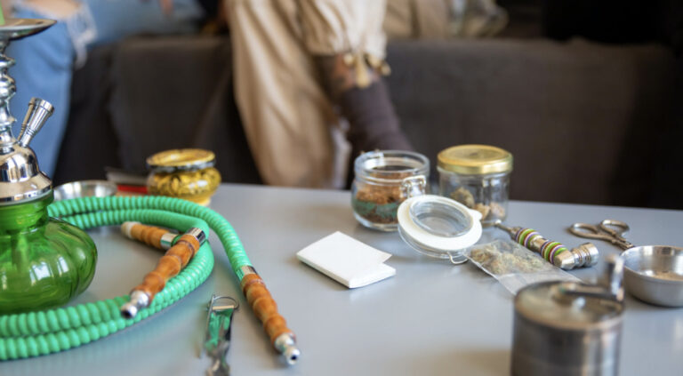 A green hookah and hose with all sorts of accessories on a table.