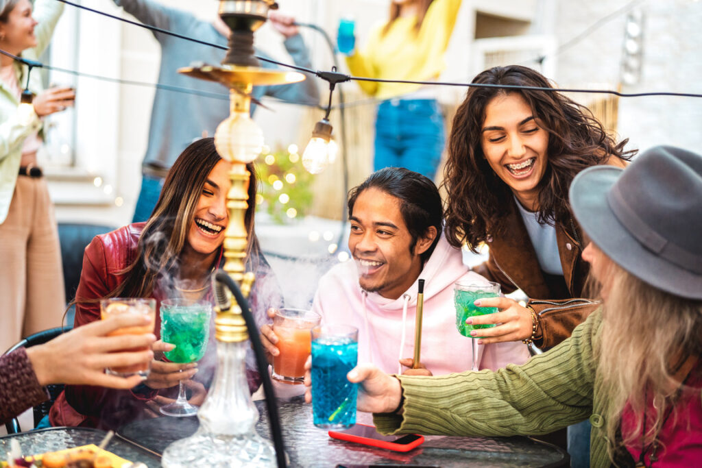 Happy trendy friends having fun drinking cocktail at hookah bar