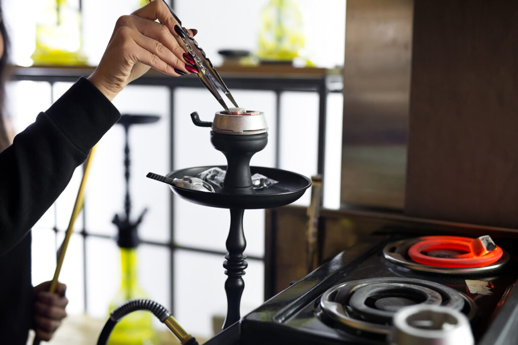 Women's hands hold hookah tongs and adjust the hot coals in a metal bowl.